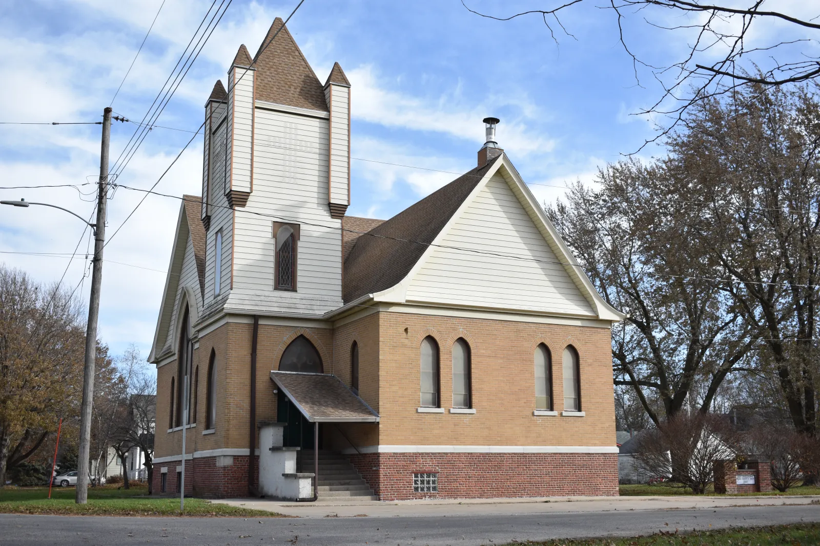Mitchellville First Congregational Church today: the cream-brick church with its white steeple, arched windows and covered entry steps on the corner, under a blue autumn sky